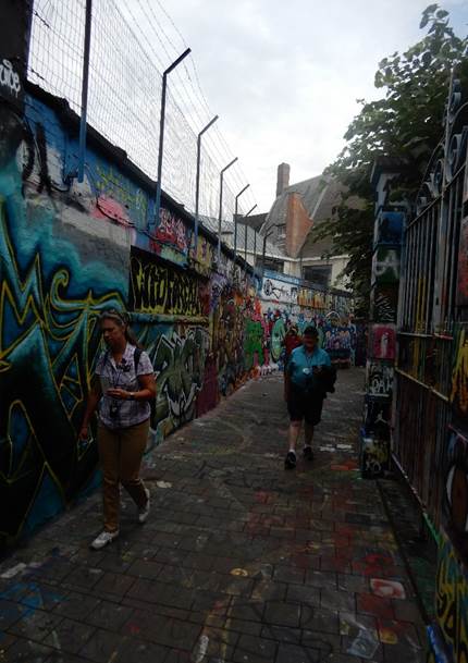 A couple of people walking on a sidewalk next to a wall with graffiti

Description automatically generated with low confidence